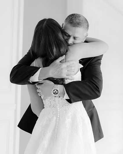 Black and white photo of a man in a suit hugging a woman in a wedding dress with their eyes closed.