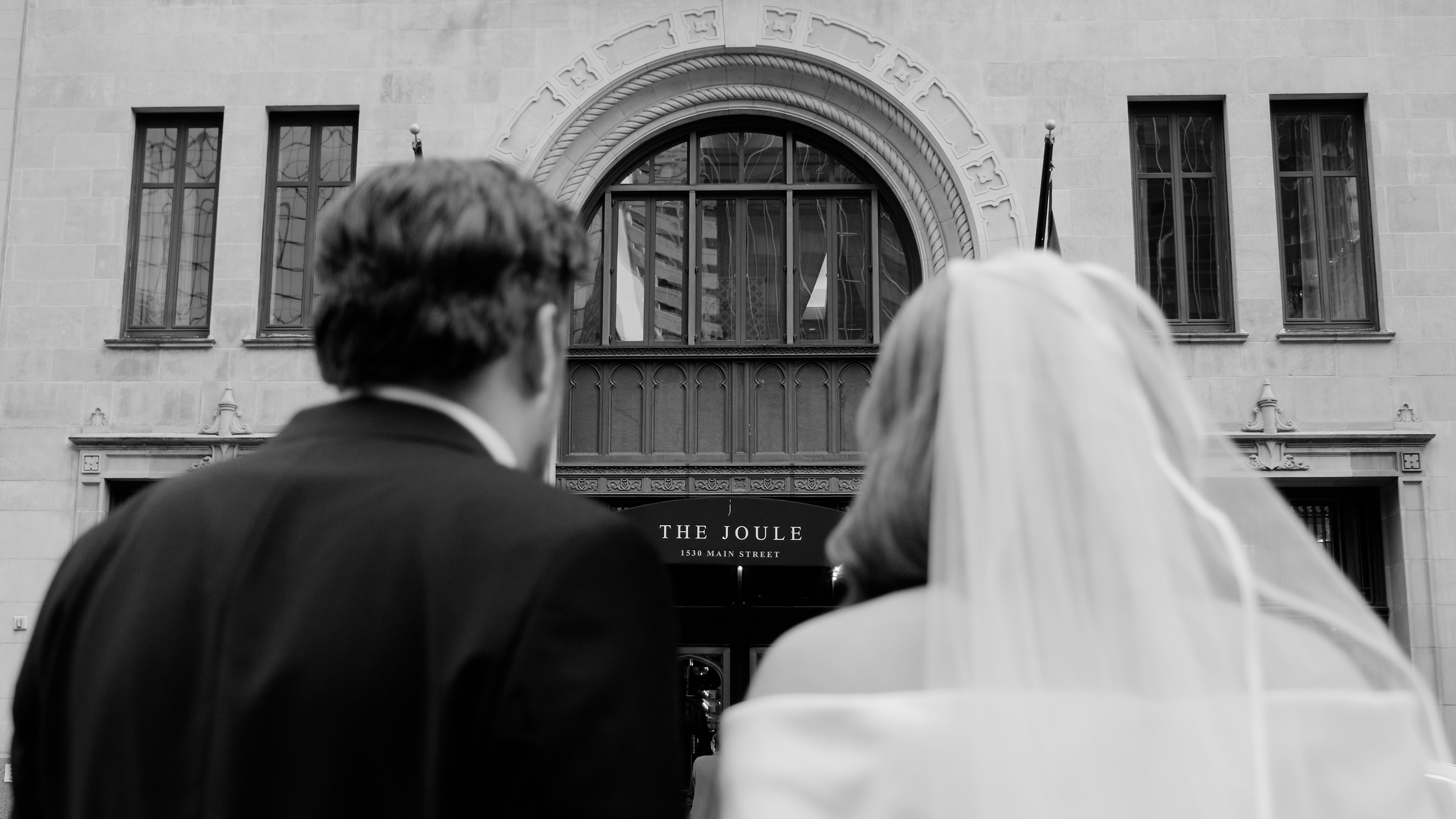 Bride and groom standing close on a decorative staircase with floral mural background, smiling at each other.