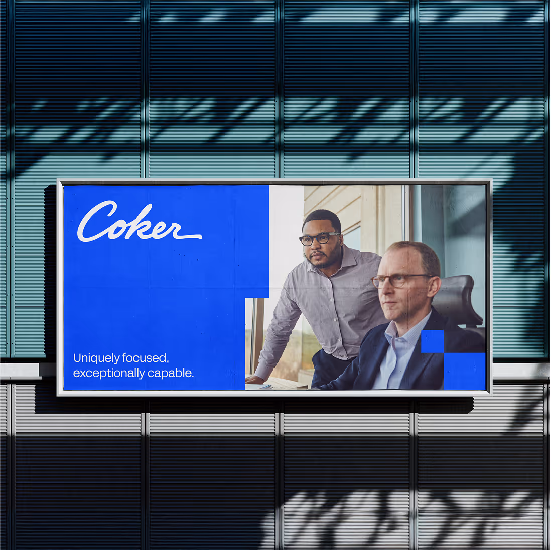 Outdoor billboard with the text 'Coker' and 'Uniquely focused, exceptionally capable' featuring two professional men in a meeting room.