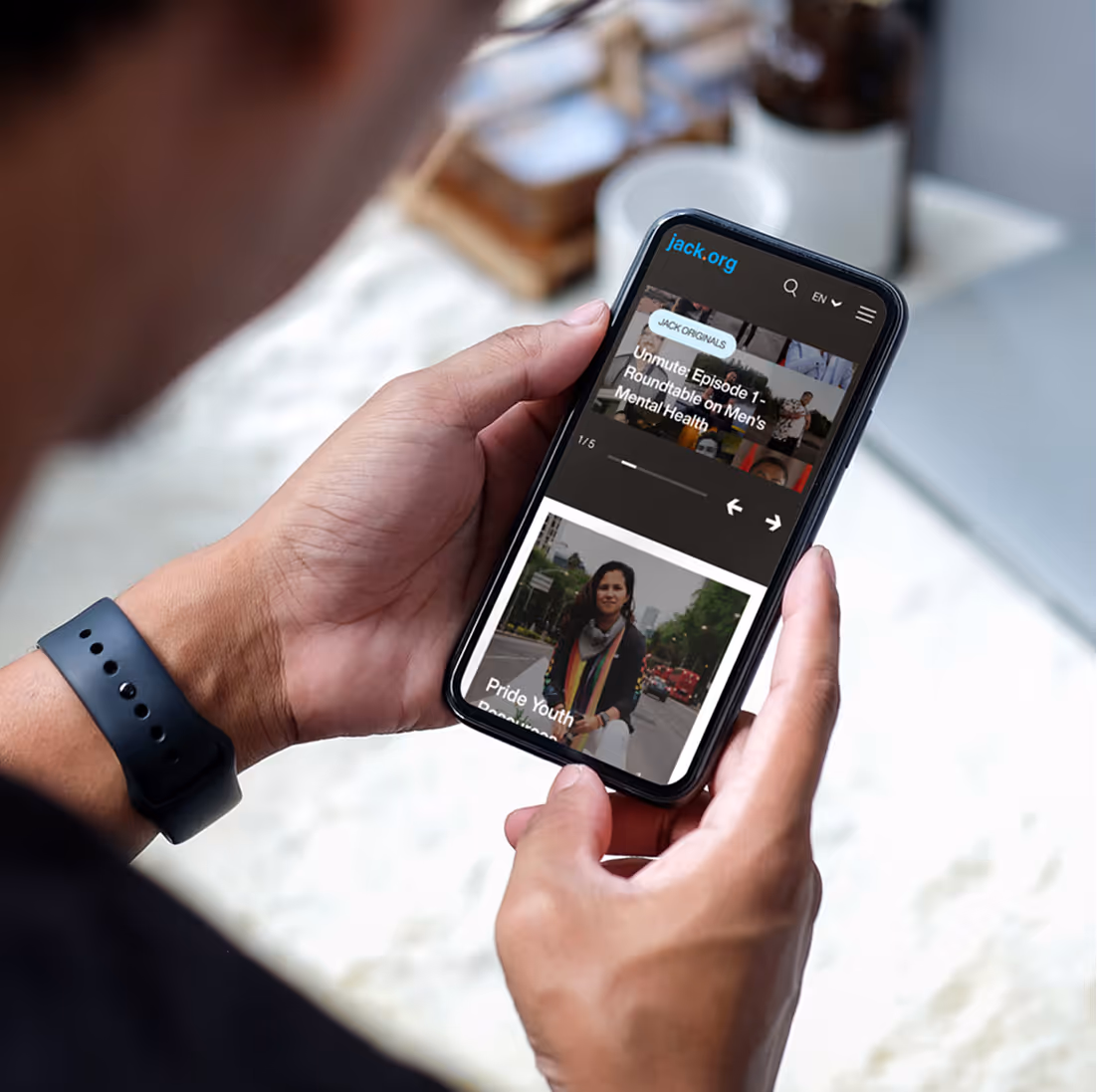 Person holding a smartphone displaying jack.org website with mental health and pride youth content.