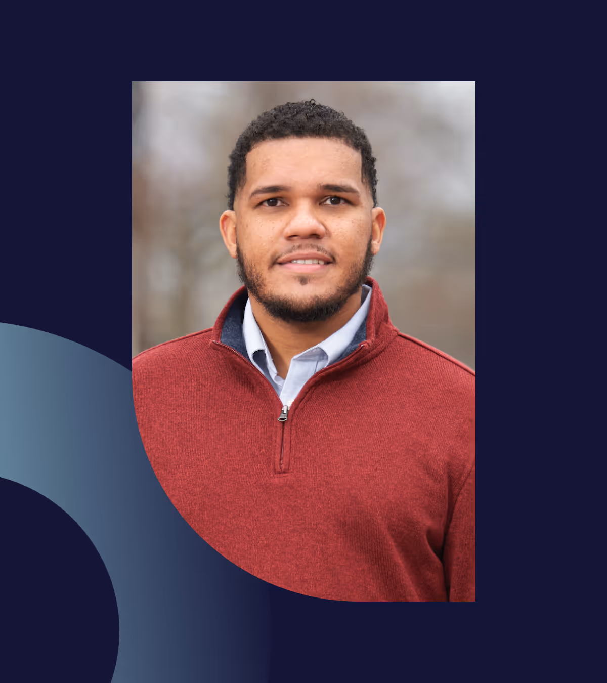 Portrait of a man with short curly hair and beard, wearing a red quarter-zip sweater over a light blue collared shirt.