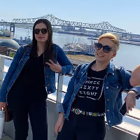 Hailey and Brittany wearing sunglasses and casual clothes posing on the Baton Rouge waterfront with a the bridge in the background.