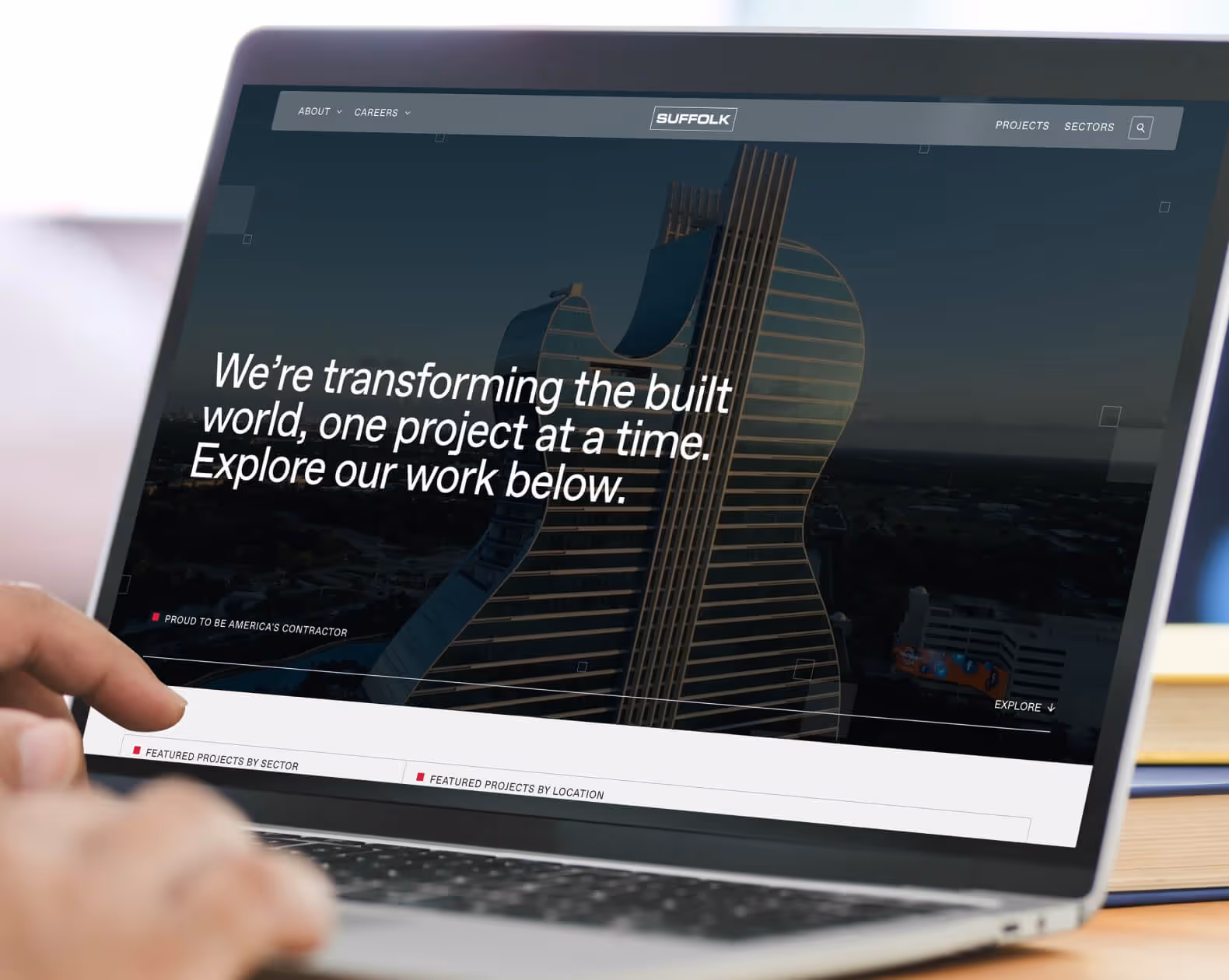 Laptop screen showing Suffolk Construction website with a unique guitar-shaped building and text about transforming the built world.