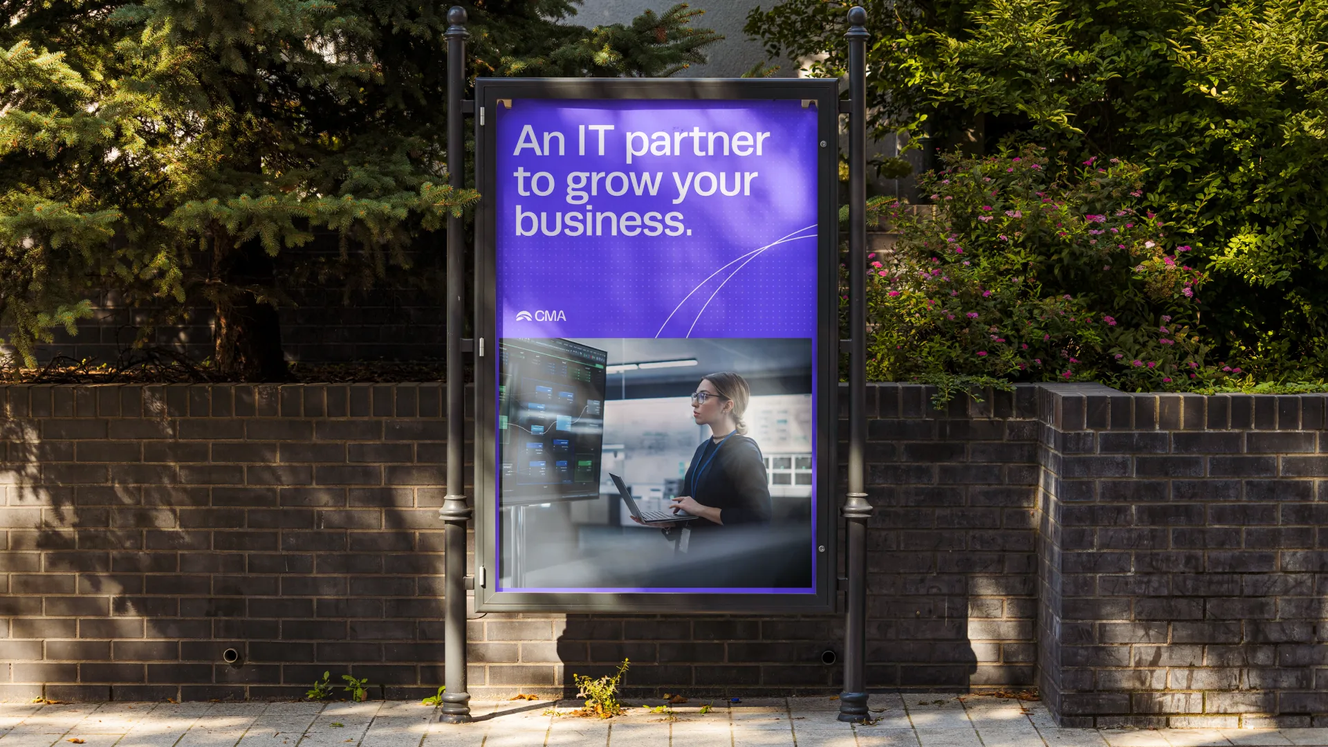 Outdoor advertisement with text 'An IT partner to grow your business' above an image of a woman working on a laptop in front of a computer monitor.