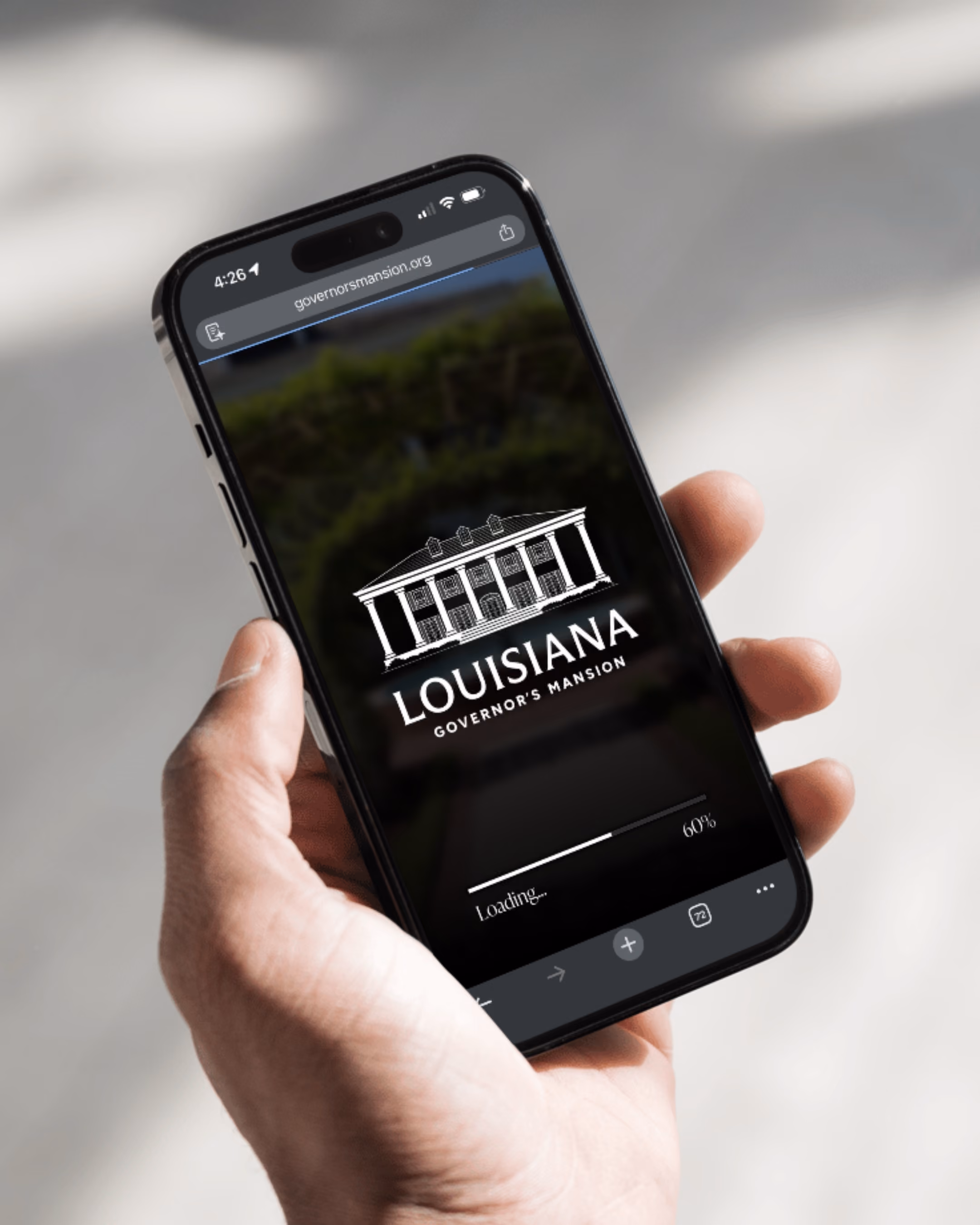 Hand holding smartphone displaying Louisiana Governor's Mansion website with loading bar at 60%.