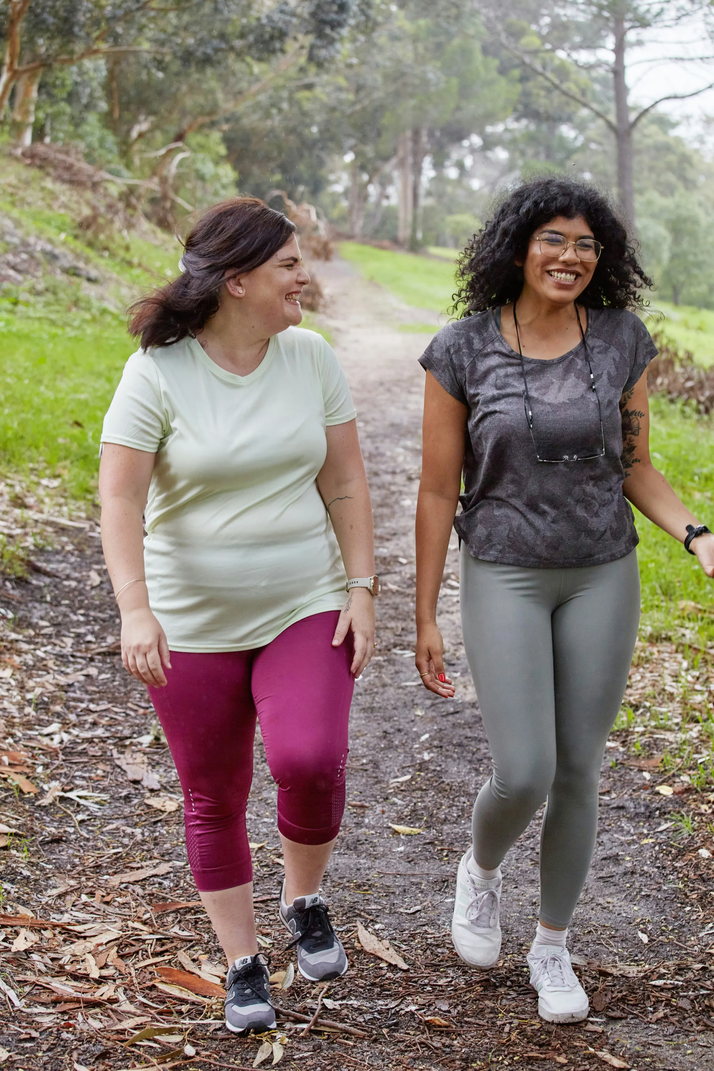 Two women smiling and walking on a forest trail.