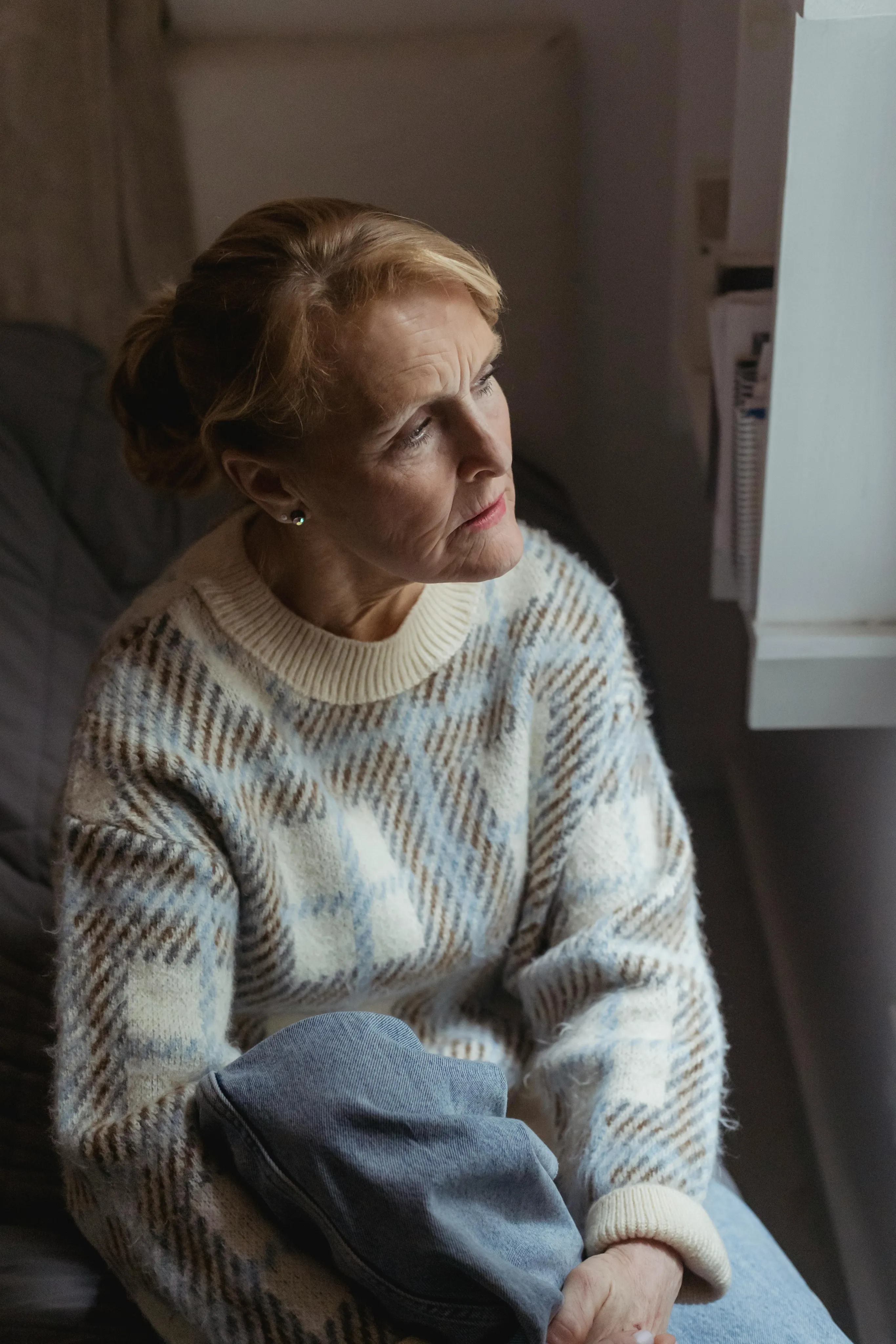 Older woman looking thoughtfully out a window.