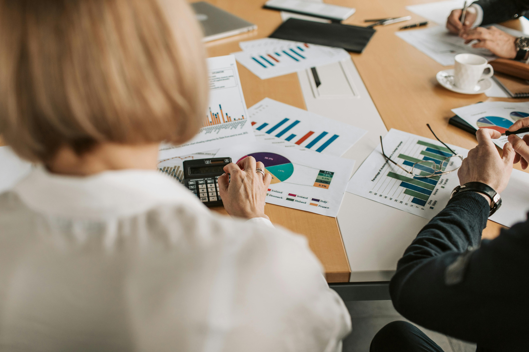 Two people at a table analyzing financial charts and graphs with a calculator and a cup of coffee.