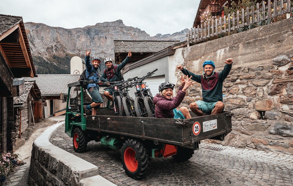 Mountain bikers on the back of a truck shuttling up in an Alpine village