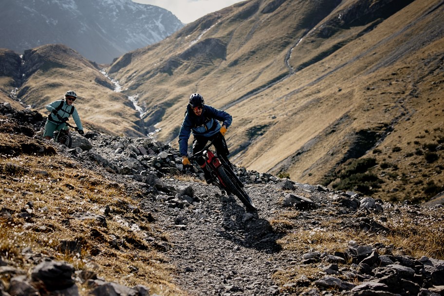 Two riders (man and woman), descending on rocky, alpine trail in Grisons