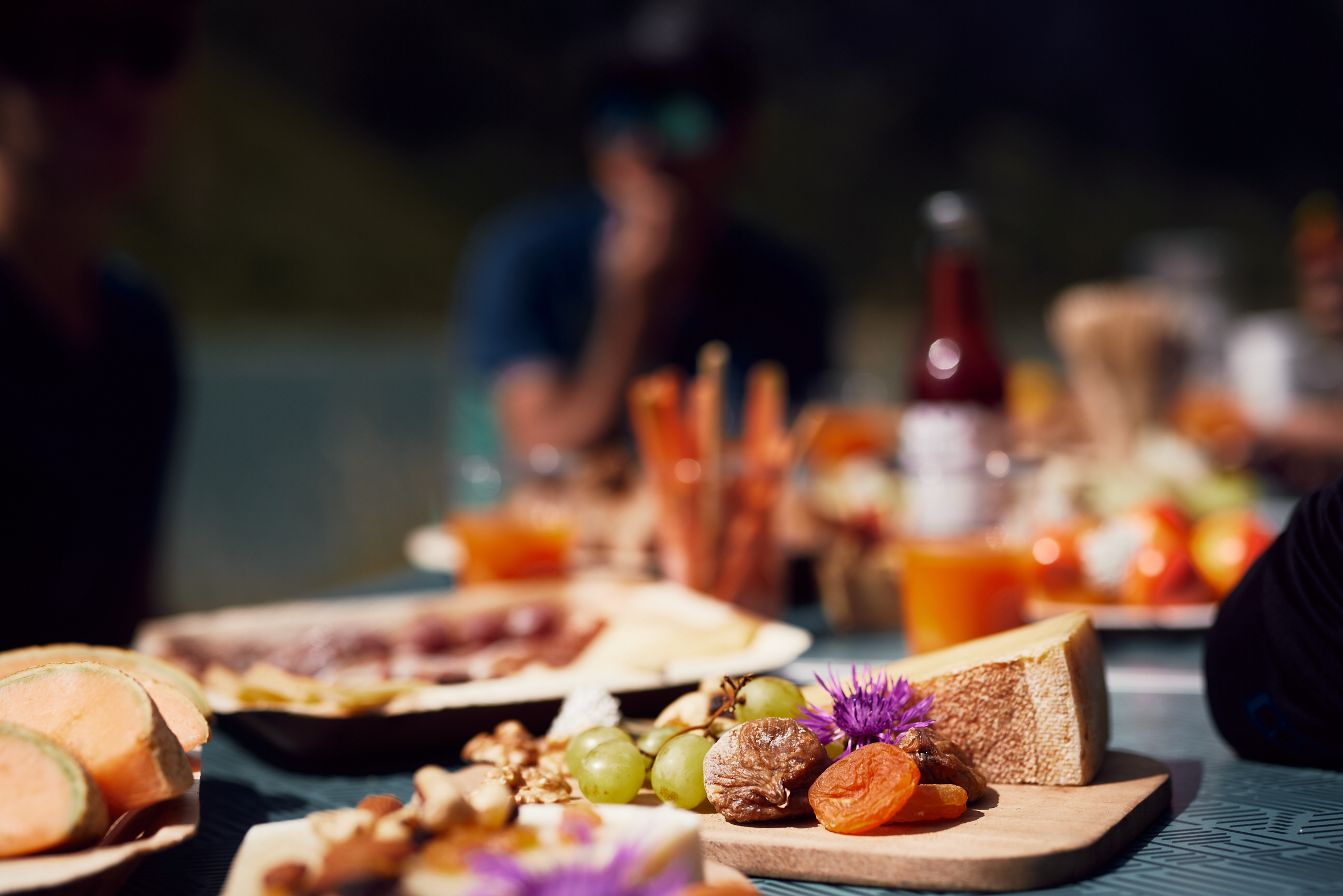 A colorful picnic table with assorted cheese, dried meats and fruits.