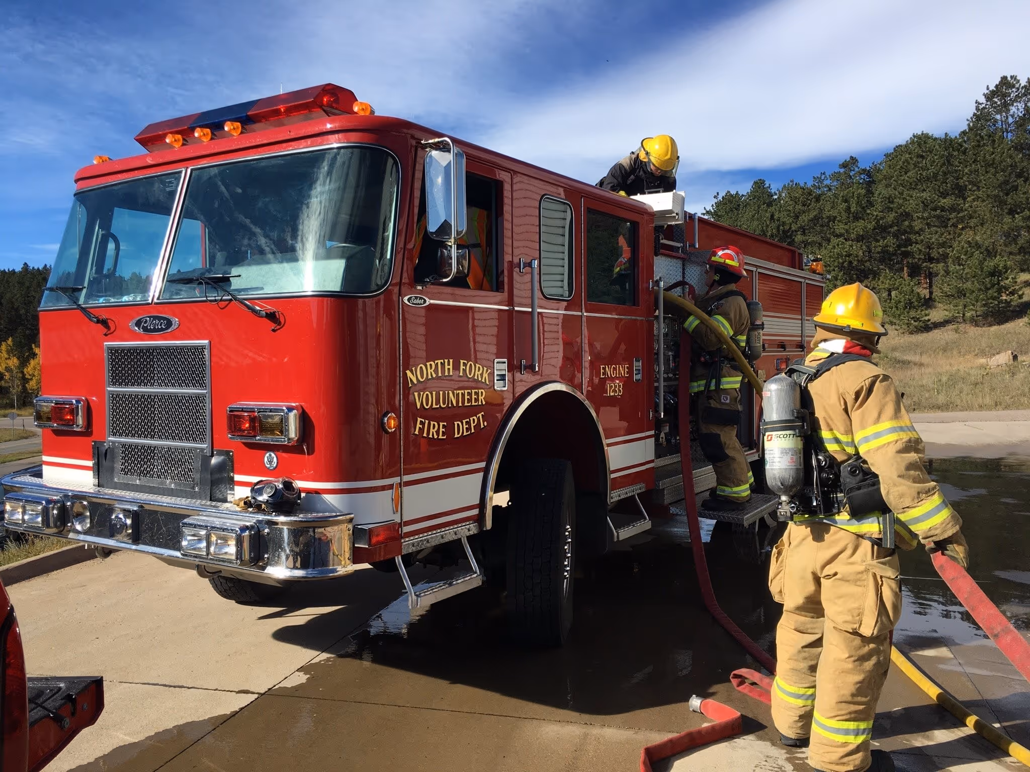 North Fork Volunteer Fire Department firefighters connecting hoses to a red fire engine during training.