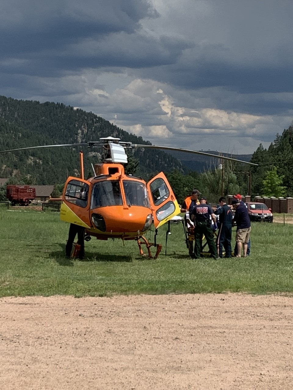 Emergency responders loading a patient into an orange medical helicopter in a grassy field.