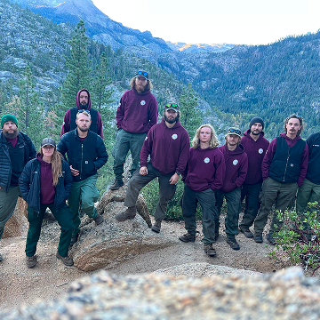 Wildland firefighting team posing together on a rocky mountain trail surrounded by trees.