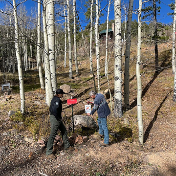 Fire department personnel helping a homeowner install a reflective address sign in a wooded area.