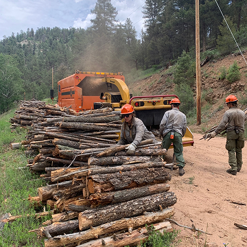 Fire mitigation crew feeding logs into a wood chipper along a mountain road.