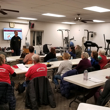 Fire department representative teaching a safety class to community members indoors.