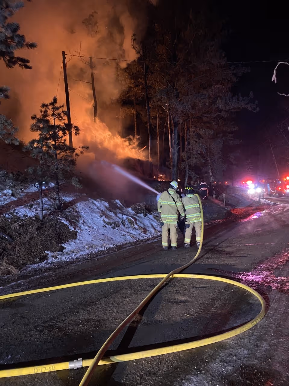 Firefighters spraying water on a nighttime wildfire burning along a wooded hillside.