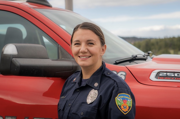 Female firefighter standing beside a red fire department truck smiling outdoors.