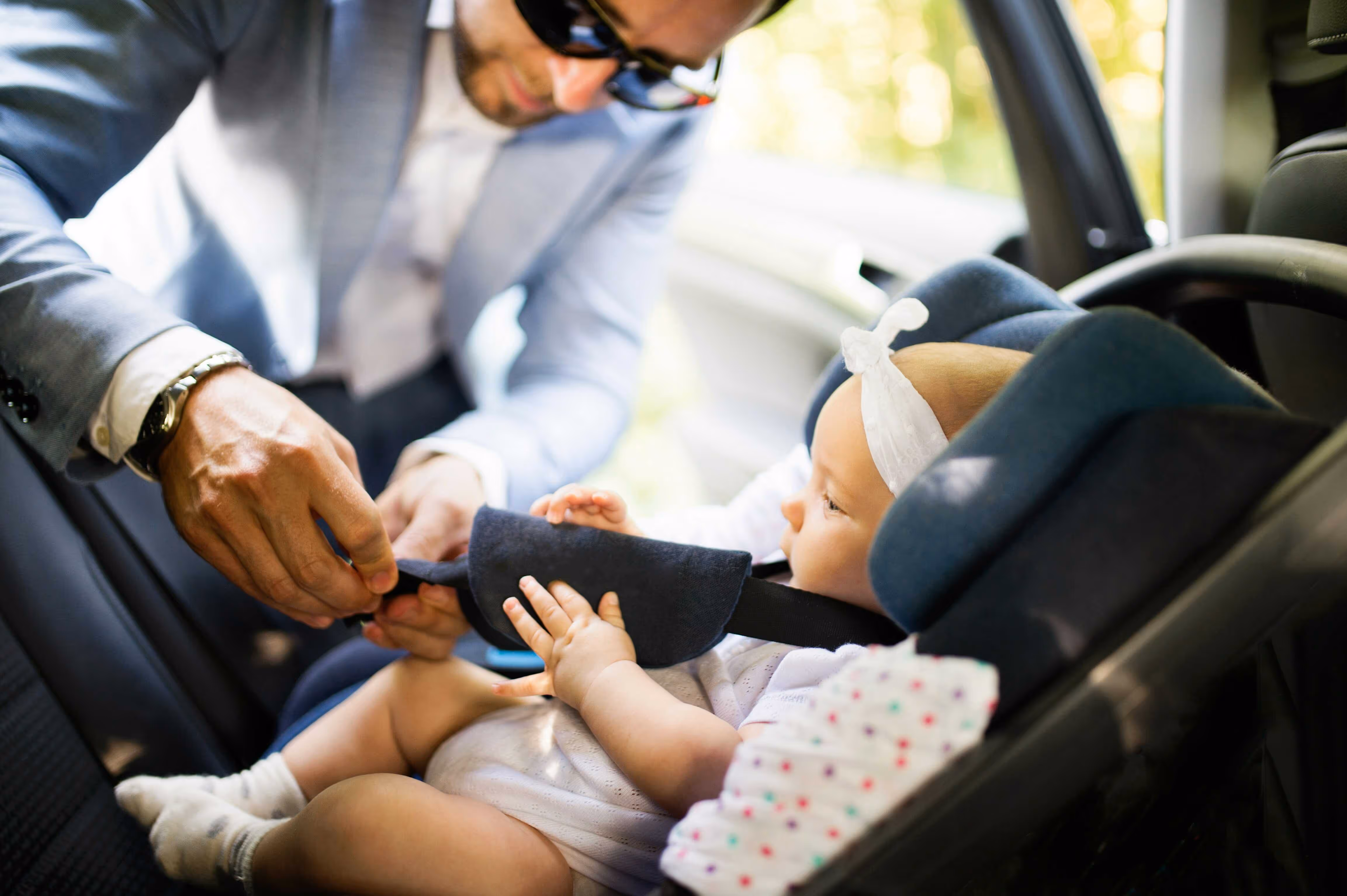 Parent securing a baby in a rear-facing car seat inside a vehicle.