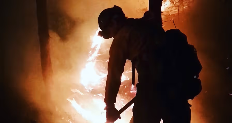 Wildland firefighter using hand tools to control an intense forest fire at night.