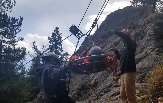 Rescue workers conducting a high-angle rope rescue, lowering a patient in a stretcher down a rocky cliff.