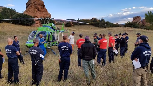 Firefighters gathered around a green helicopter during a field training exercise.