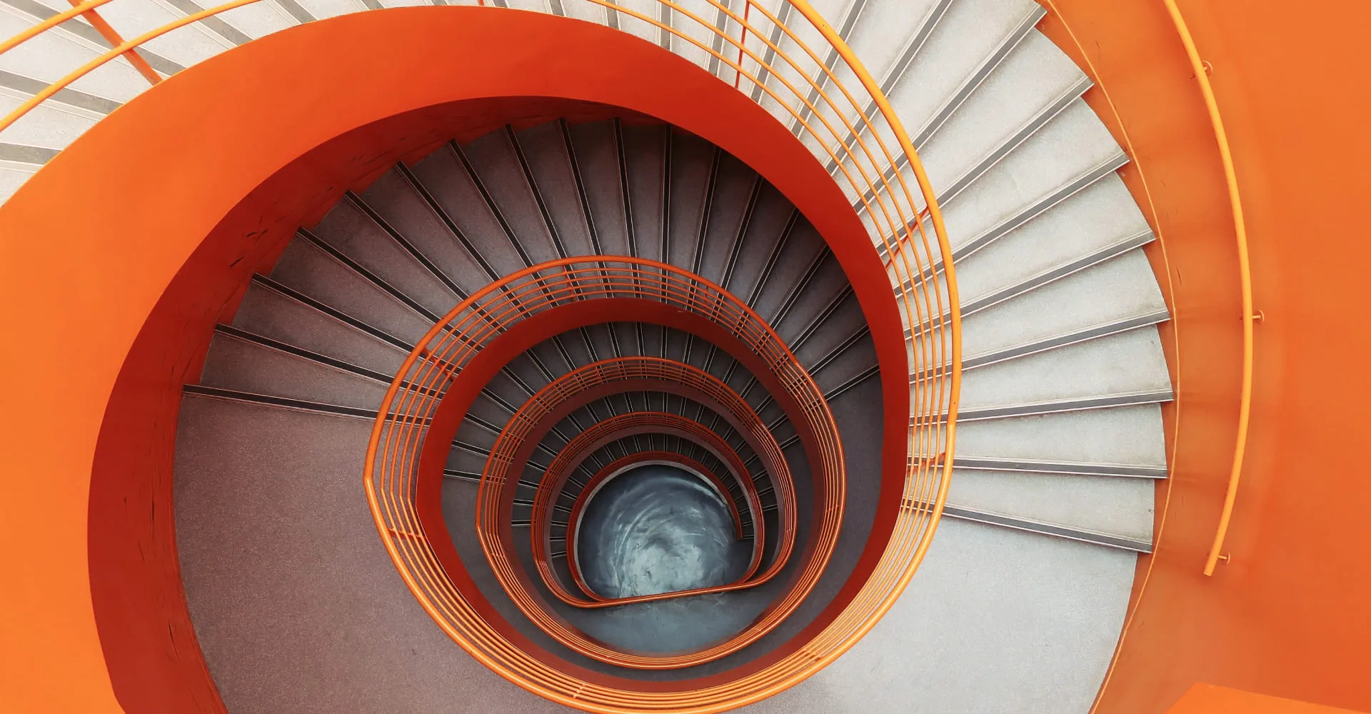 Top-down view of a spiral staircase with bright orange railings and light gray steps.