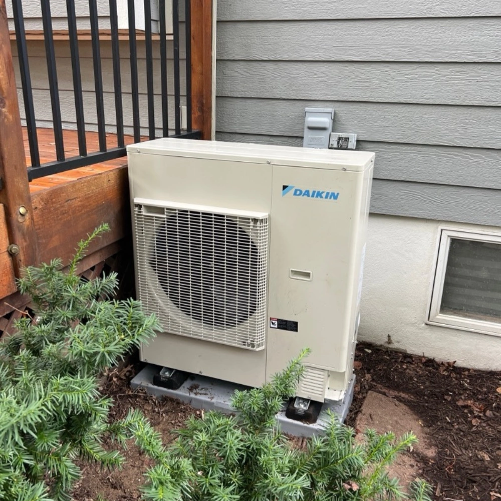 Air conditioning unit labeled "Daikin" outside a house, placed on a concrete pad.
