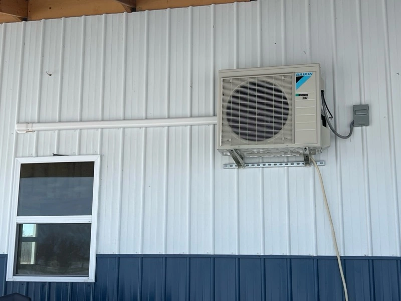 Outdoor air conditioning unit on a white metal siding wall above a window. 