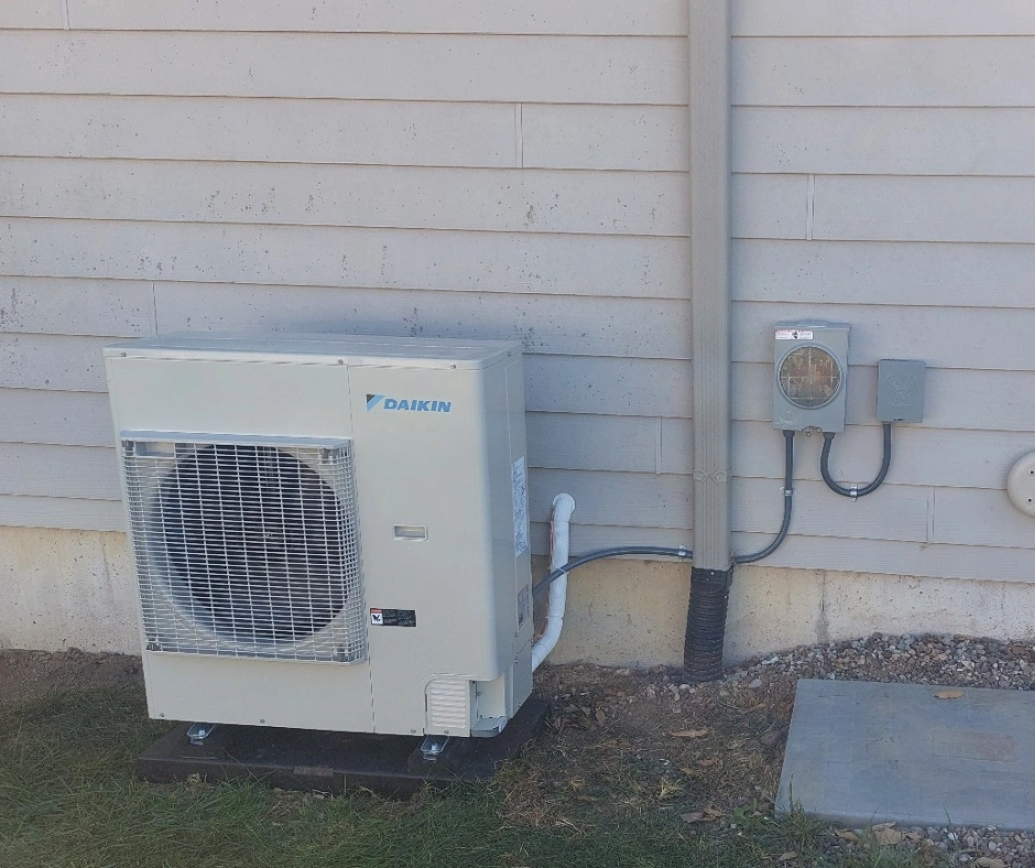 Outdoor air conditioning unit mounted on a concrete base against a beige wall. 