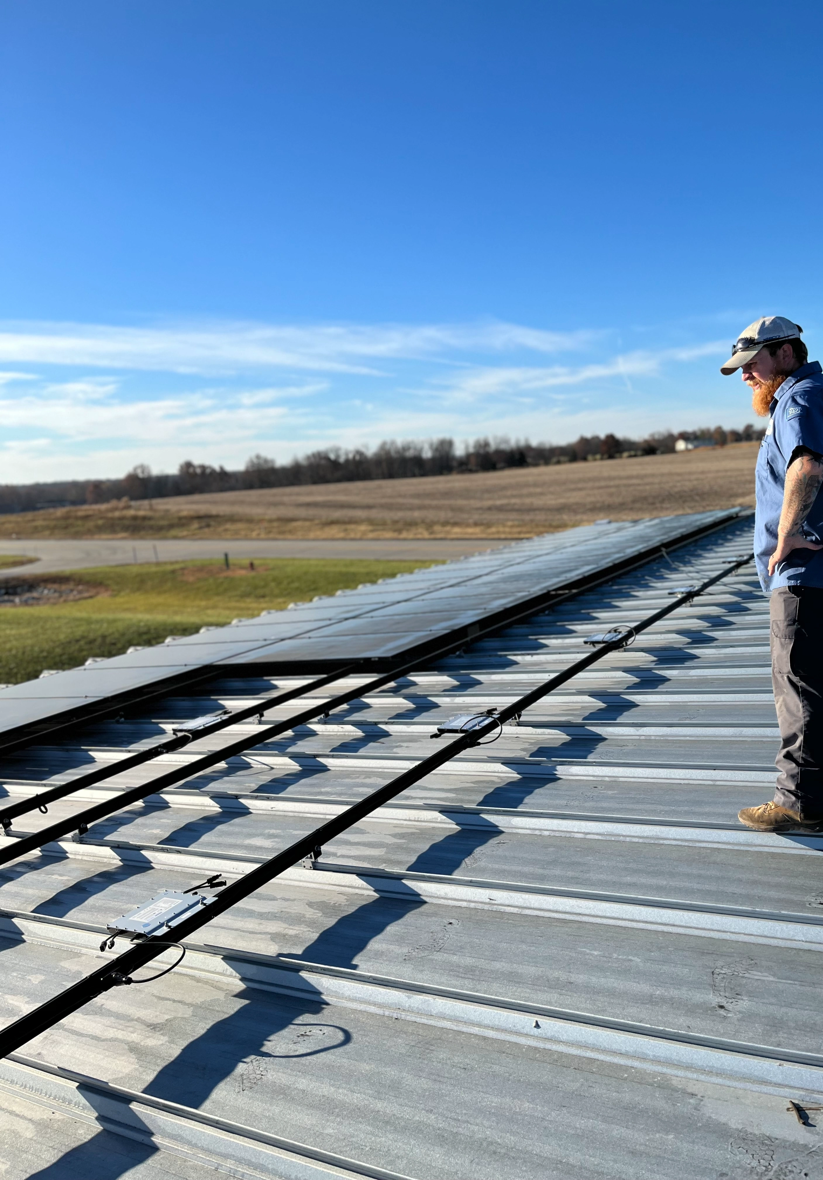 A person standing on a metal roof in sunlight, gazing out at open fields under a clear blue sky. 