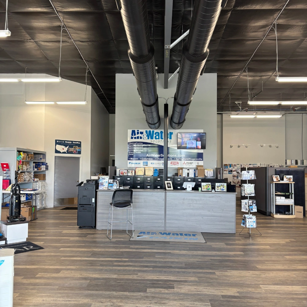 Office reception area with high ceilings and exposed black ductwork. A counter with brochures and a TV is present. 