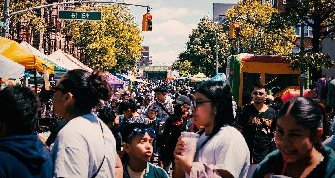 Crowded street fair on 61st Street with people walking among tents, food stalls, and a bounce house under sunny weather.