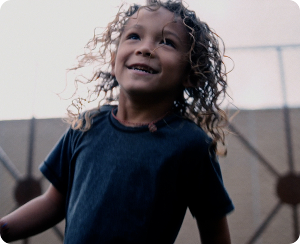 Smiling child with curly hair wearing a dark t-shirt outdoors.