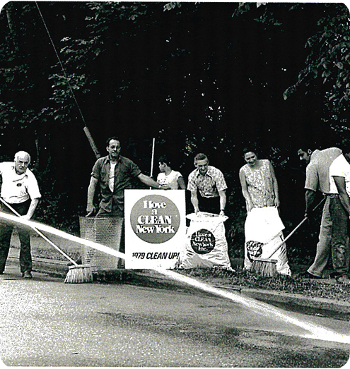Black-and-white photo of six people cleaning a street with brooms and holding 'I love a CLEAN New York' signs during the 1979 cleanup.