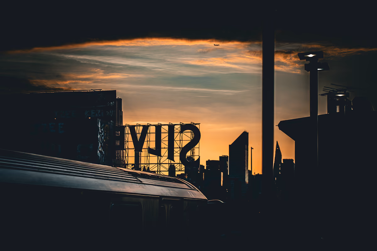 Silhouette of a city skyline at sunset with a large 'SILV' sign and an airplane in the sky.