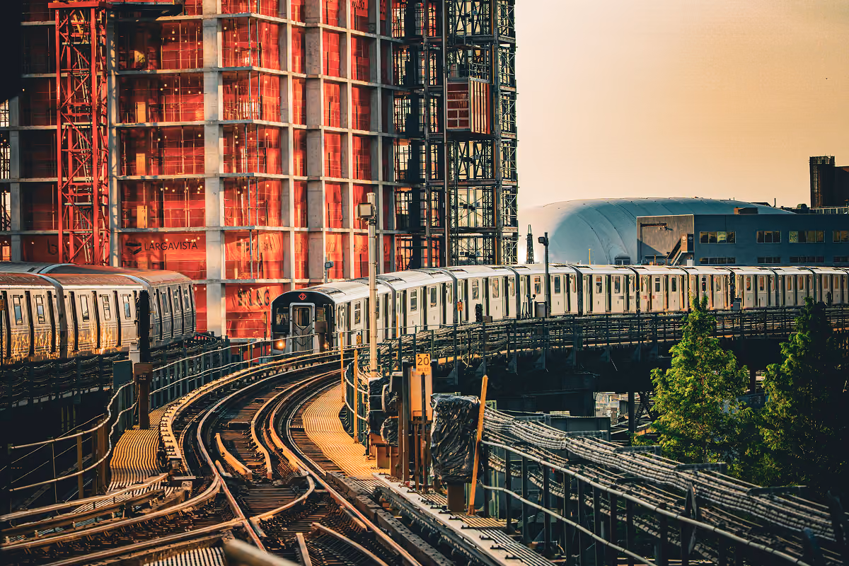 Subway train on elevated curved track passing a building under construction at sunset.