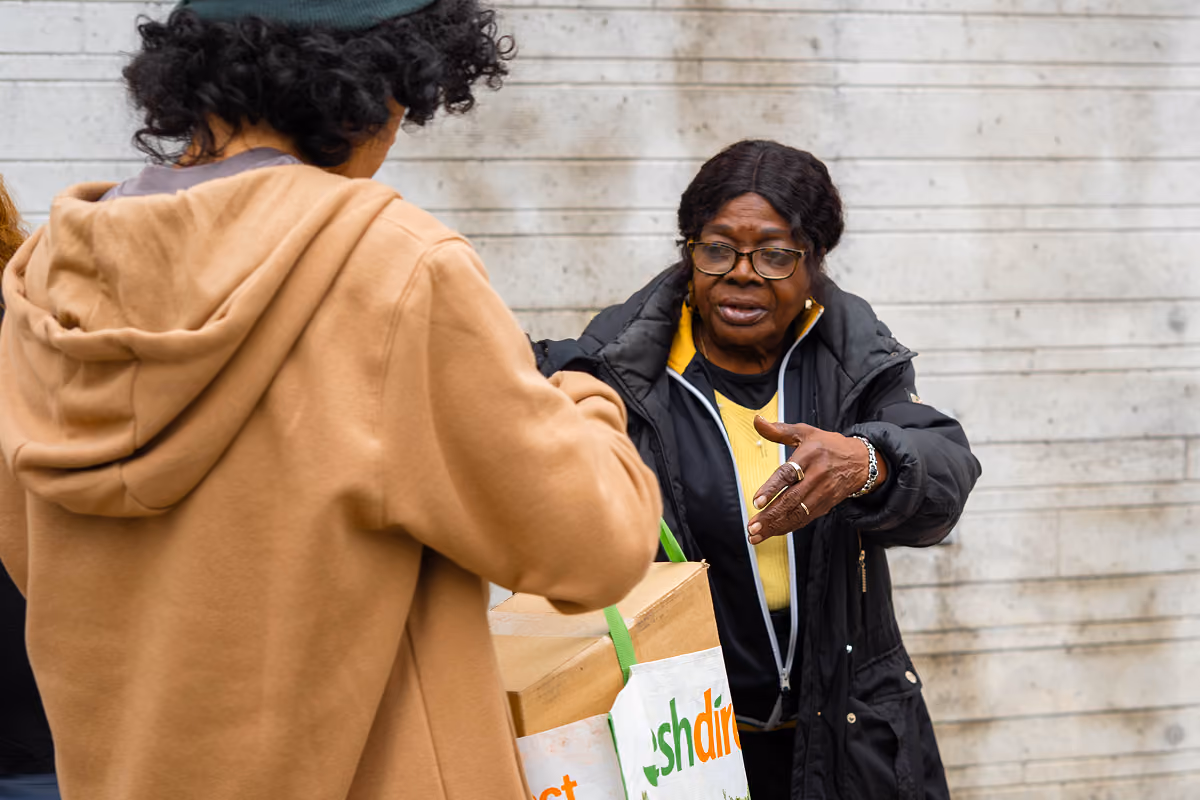 Young person handing a cardboard box to an older woman wearing glasses and a black jacket.