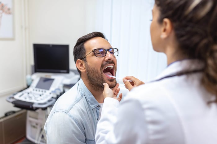 Dentist gently examining a patient's tongue with a tongue depressor during an oral health checkup. 
