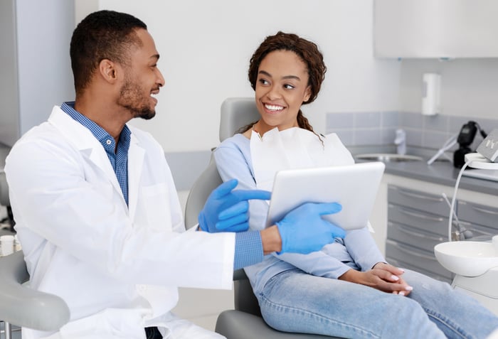 Dentist explaining an oral health concept to a patient while pointing to a diagram on a tablet.