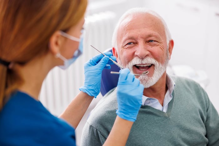 Older adult smiling at his dental hygienist during a routine cleaning appointment.