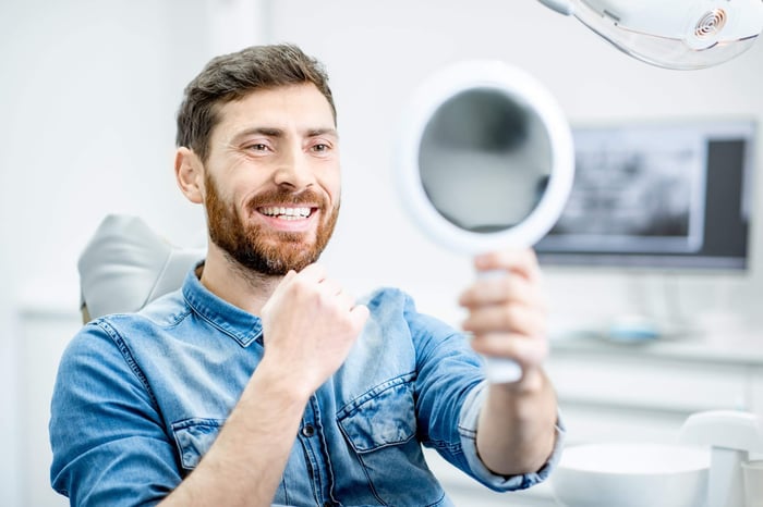 Man smiling as he looks in the mirror after having his braces removed.