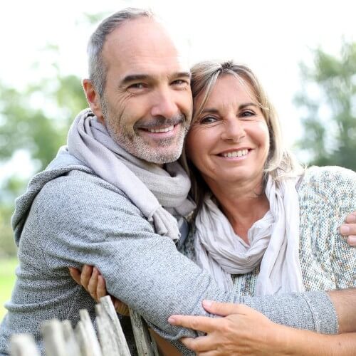 Older man smiling and hugging his wife over top of fence
