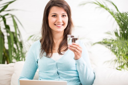 woman sitting on couch holding glass of water and laptop computer