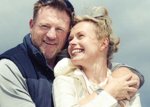Middle age couple laughing hugging on beach woman looking back
