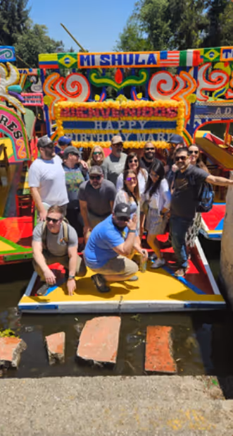 Group of people posing on a colorful decorated boat with a 'Happy Birthday Mark' sign in the background.