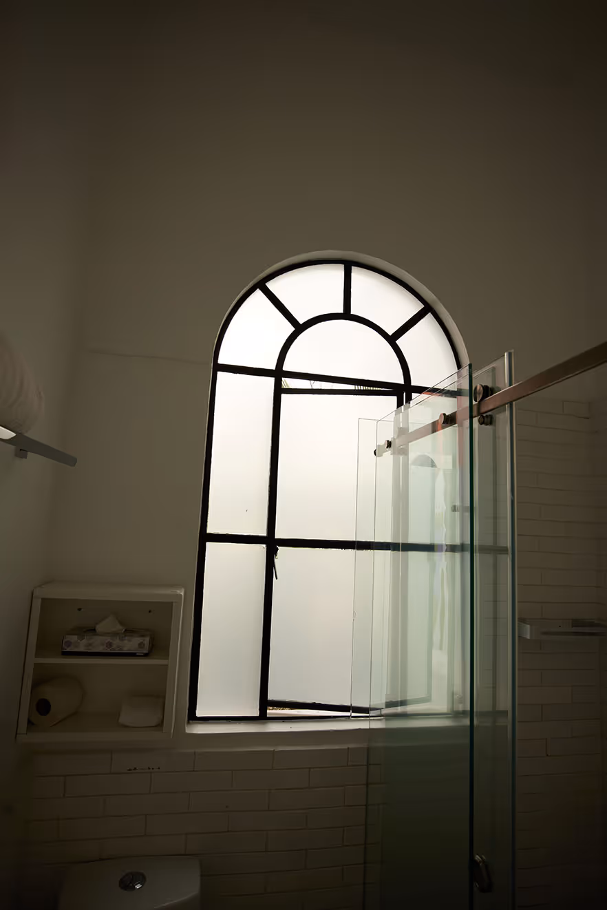 Bathroom with frosted arched window and glass shower door.