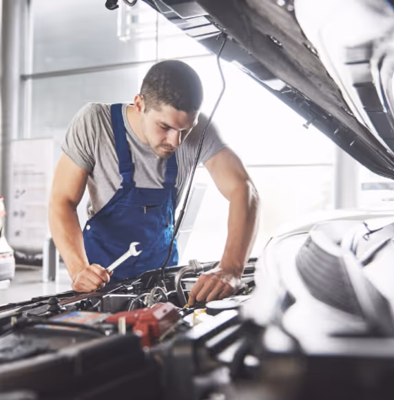 Mechanic servicing a vehicle, holding a wrench and examining the engine.