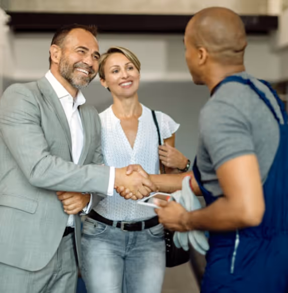 A mechanic shaking hands and speaking with two customers.